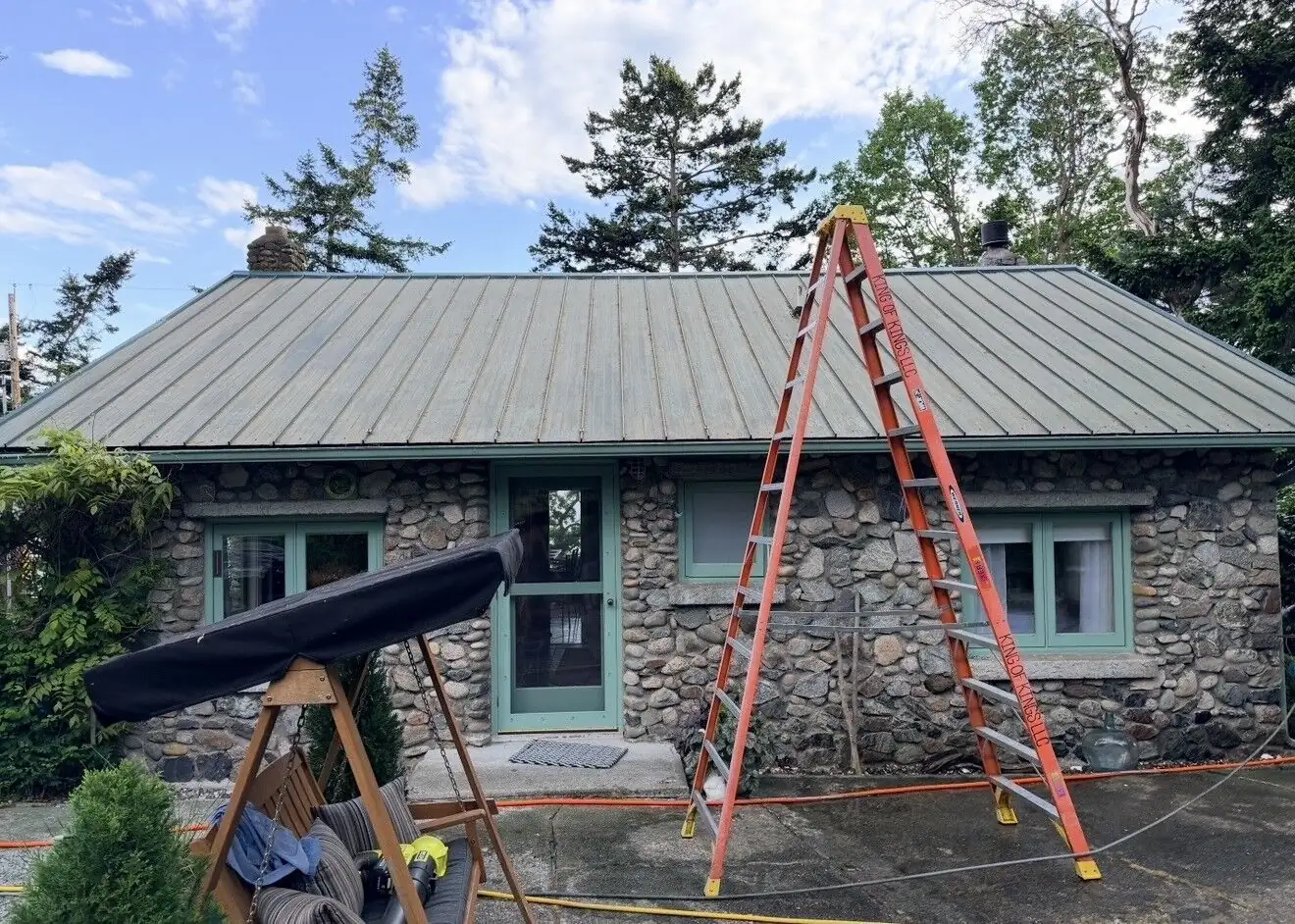 Ladder set up beside a stone home for access to the metal roof
