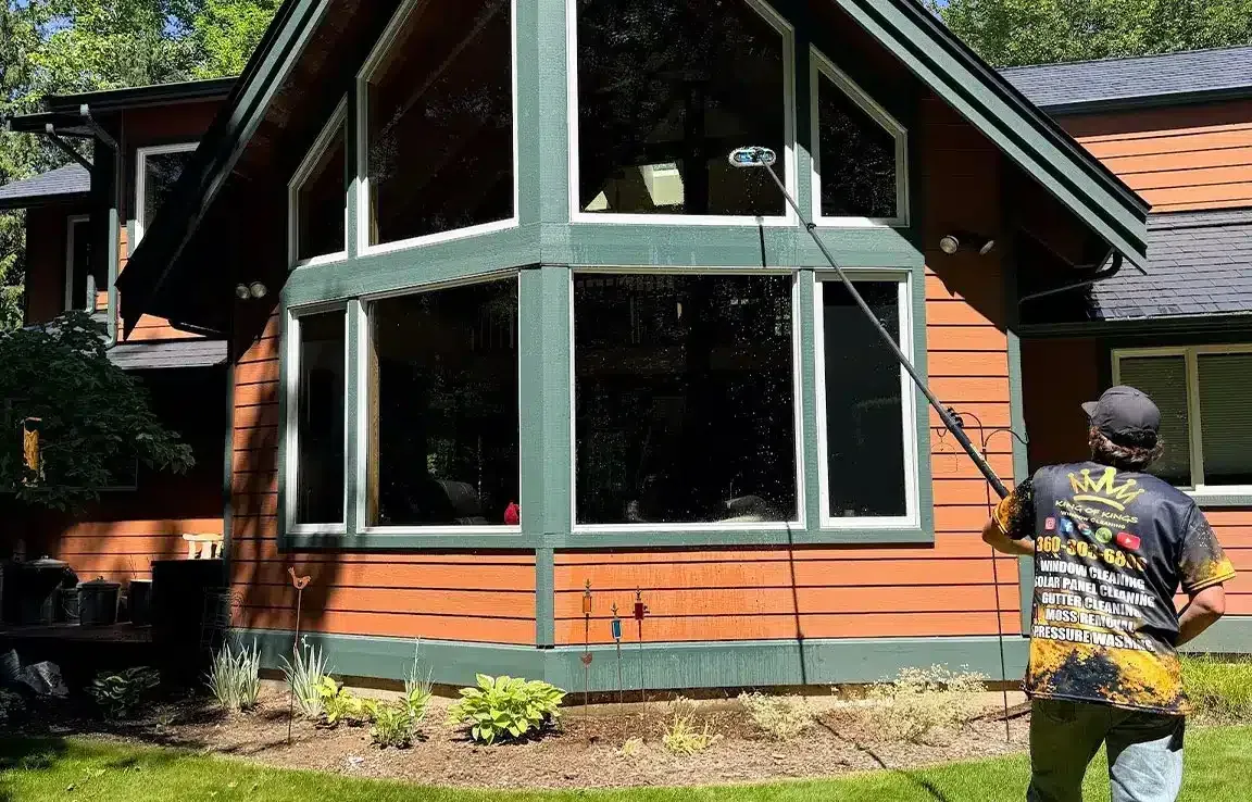 Long pole brush cleaning large multi-pane windows on a house with green trim