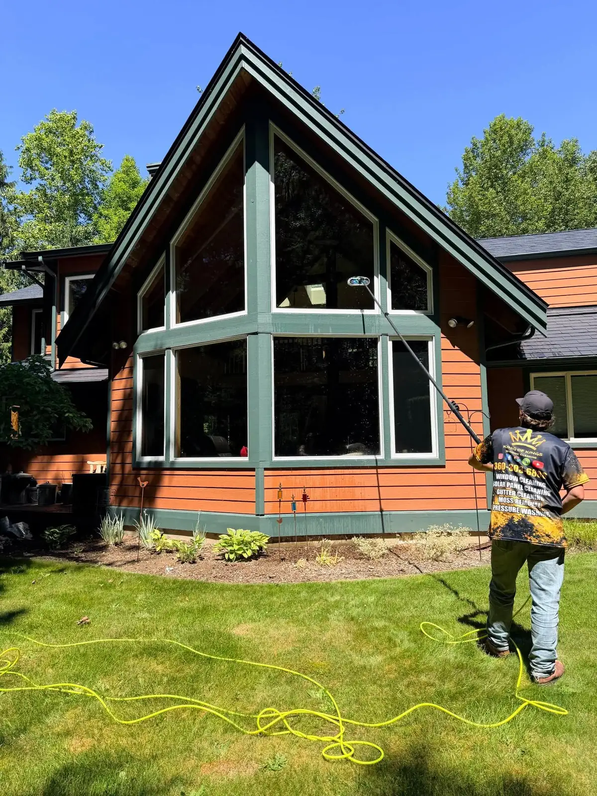 Technician using a long pole to clean large triangular windows of a house with green trim