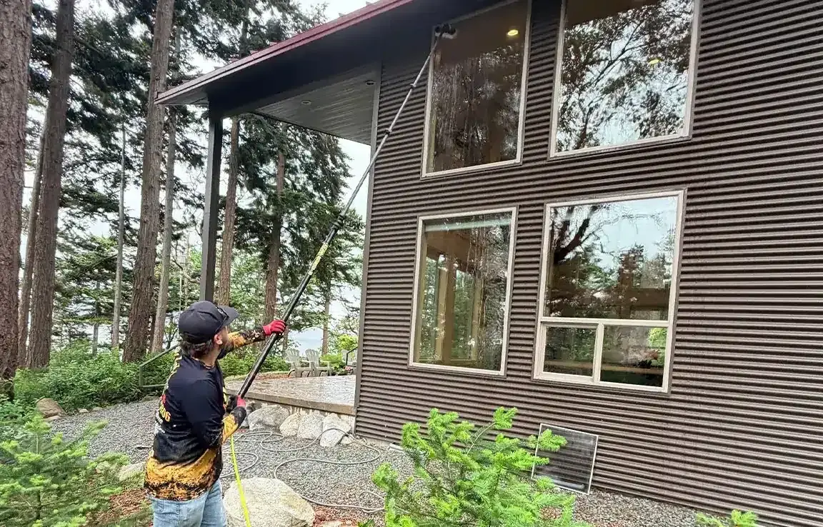 Technician using a long pole to reach upper windows of a two-storey house
