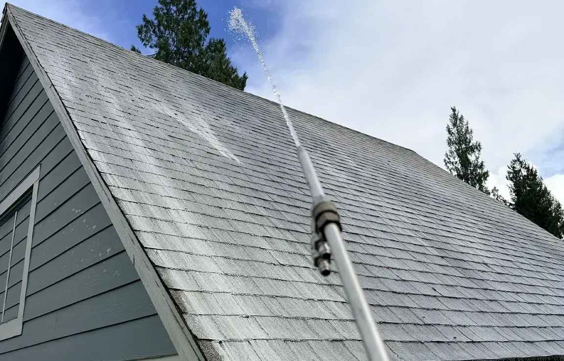 Steep gray metal shingle roof being rinsed with a low-pressure stream of water