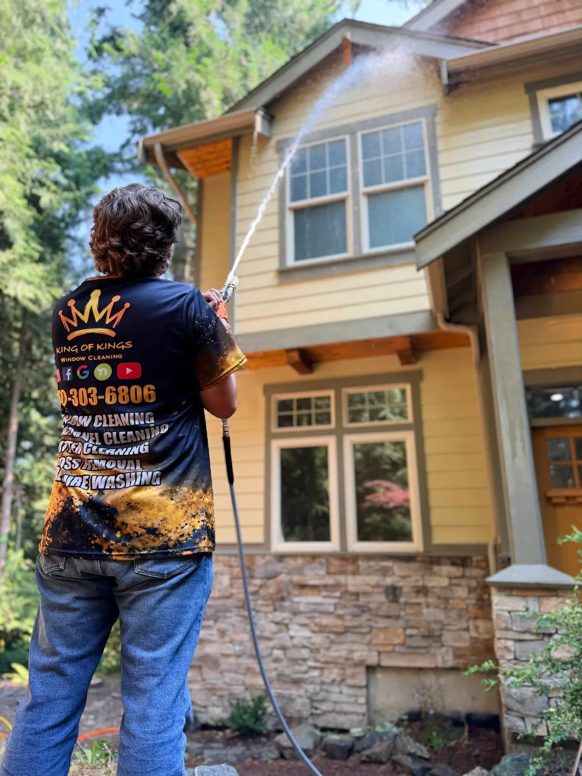 Technician rinsing second-floor windows of a two-storey home from the ground