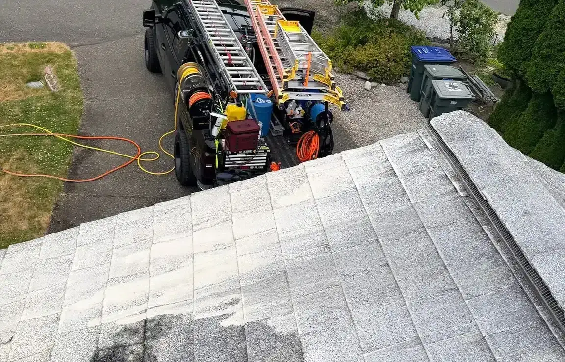 View from a roof over the shingles to a work truck in the driveway below