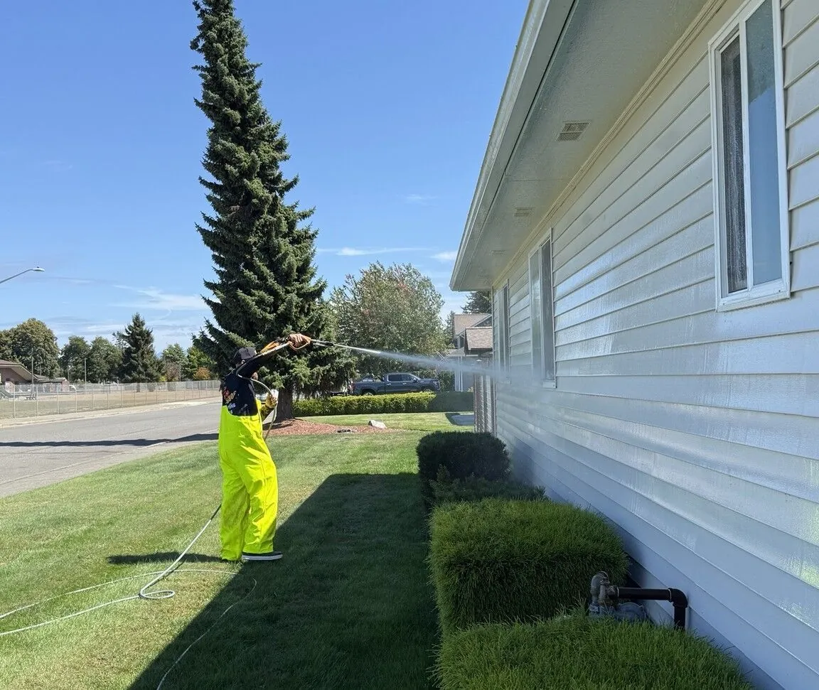 Technician soft washing the exterior wall of a home from the lawn at low pressure