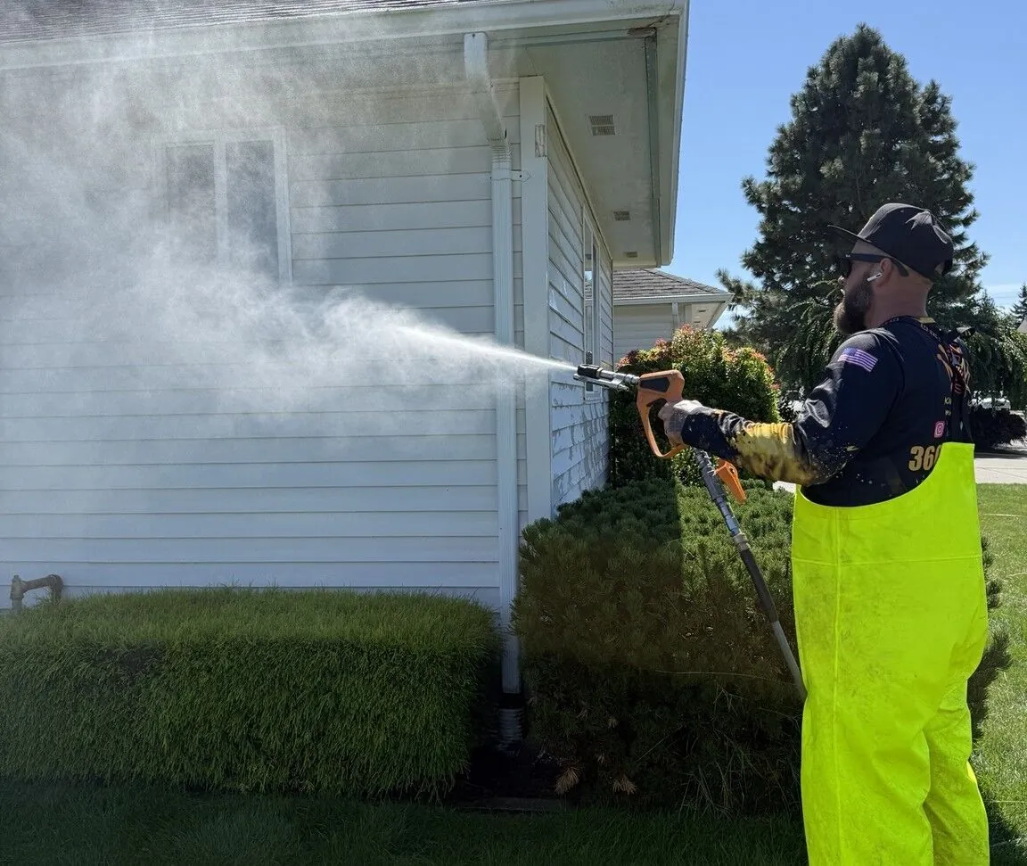 Technician applying a siding-safe soft wash solution to an upper wall