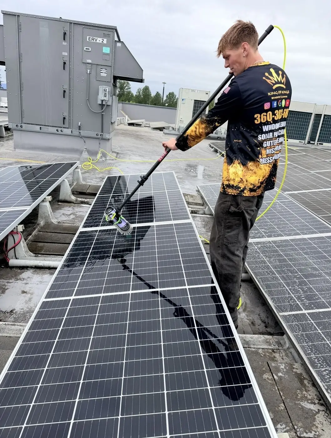 Technician cleaning solar panels with a water-fed pole on a commercial rooftop