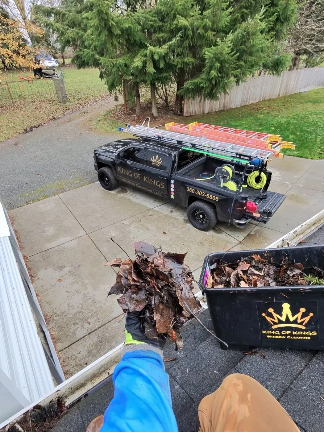 Service truck in a driveway beside a collection bin filled with debris removed from the gutters