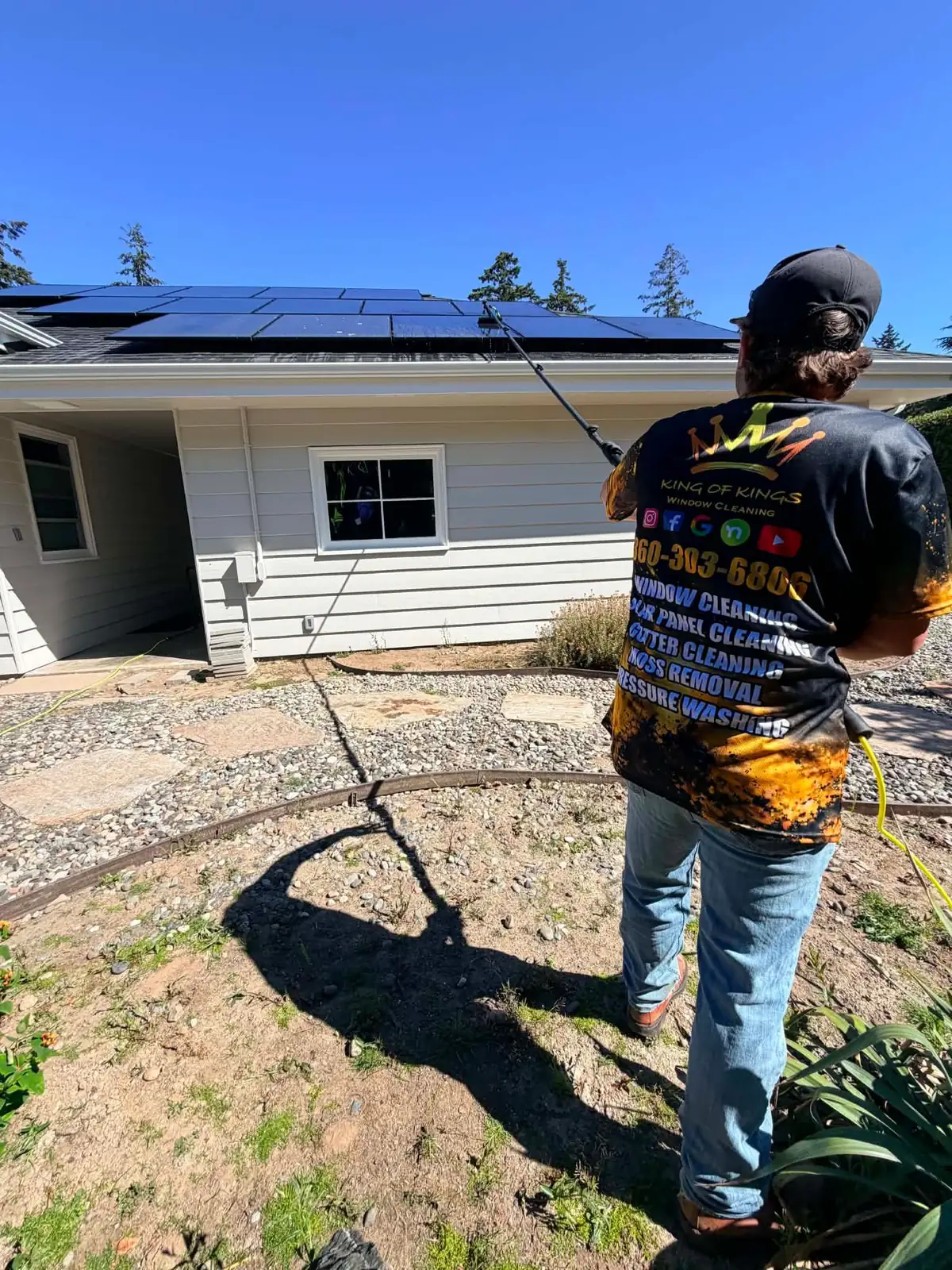 Technician cleaning a rooftop solar array with a water-fed pole beside a single-storey home