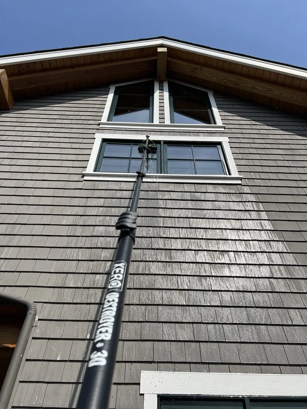 Water-fed pole reaching upper gable windows to scrub and rinse them from the ground